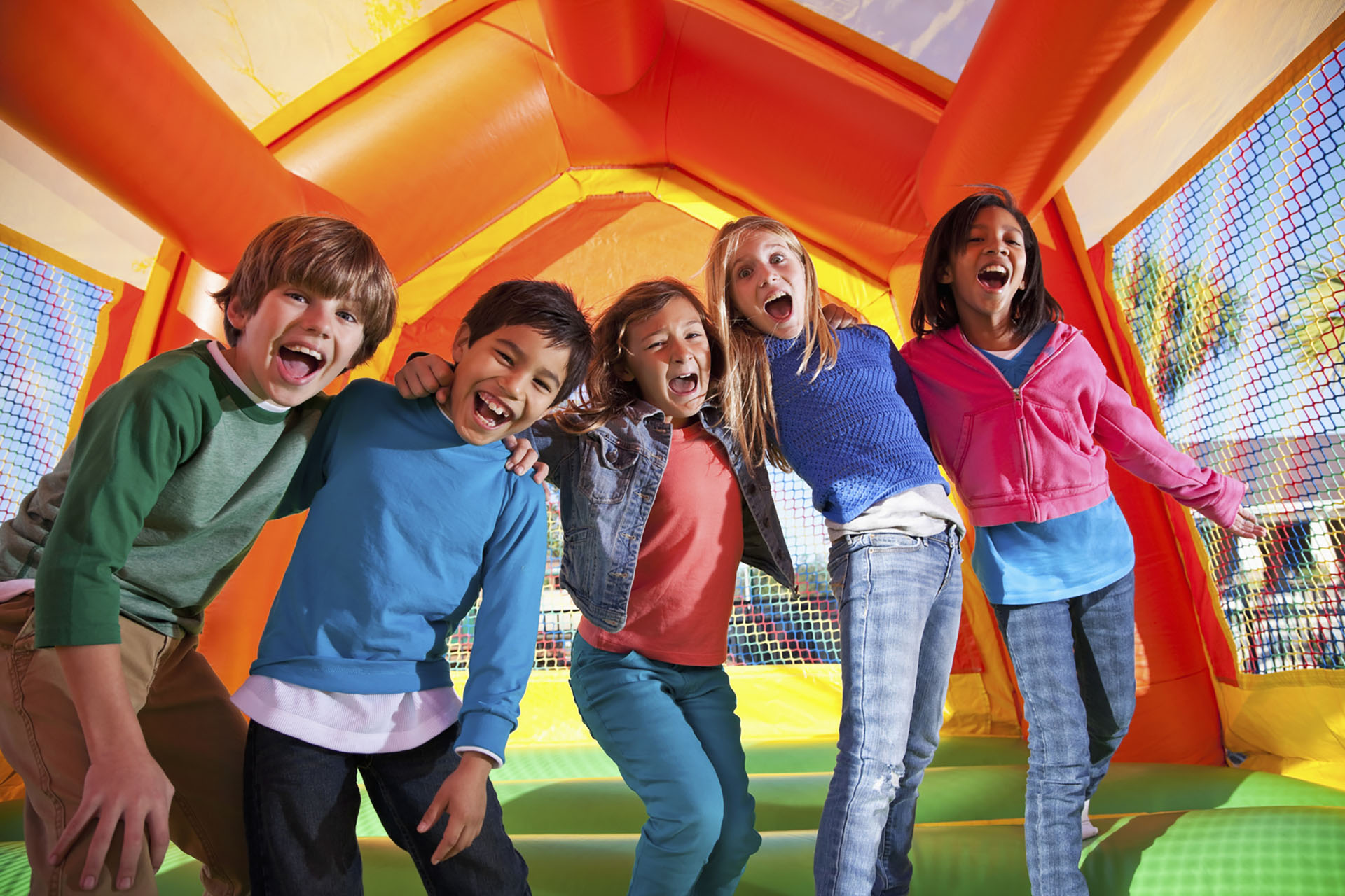 Multi-ethnic group of excited children (ages 7 to 10 years) in inflatable bouncy castle.